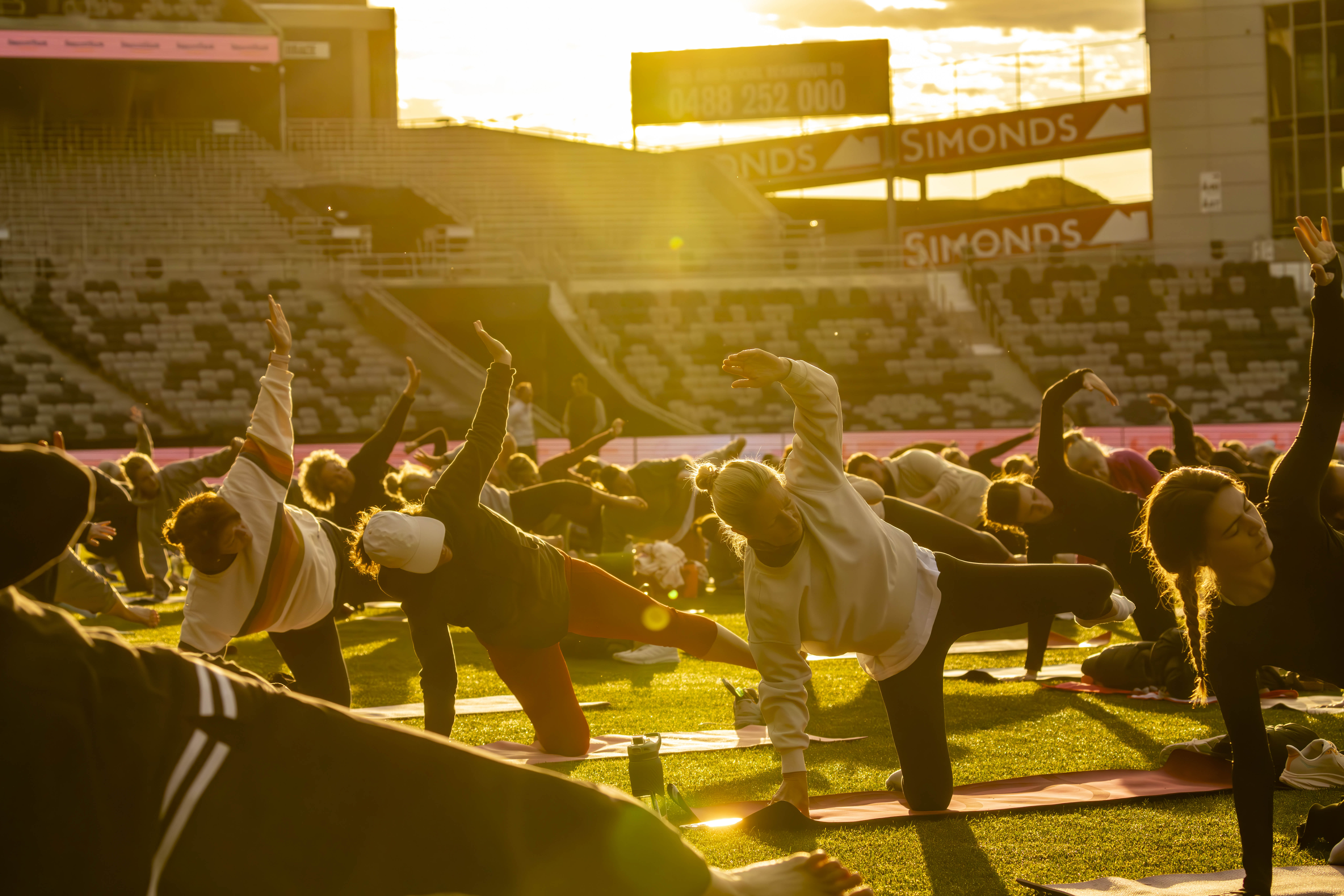 People practising yoga on the oval at GMHBA Stadium in the warm sunrise glow