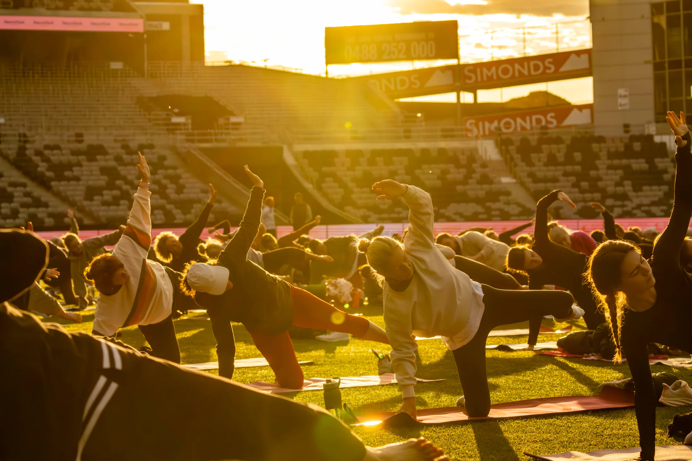 People practising yoga on the oval at GMHBA Stadium in the warm sunrise glow